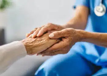 Médico segurando as mãos de um paciente idoso em um gesto de apoio e cuidado, ilustrando a importância de profissões estáveis como a medicina no Brasil.