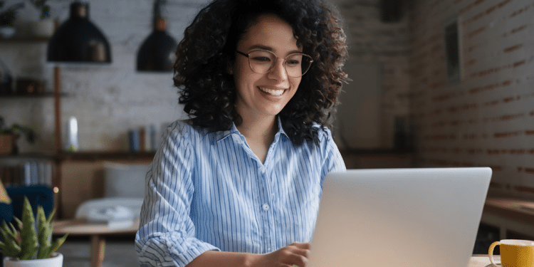 Pessoa sorrindo enquanto trabalha no computador, representando a busca por qualidade de vida no trabalho.
