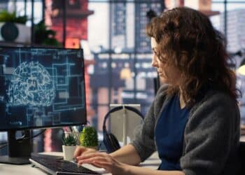 Profissional trabalhando em computador com visualização de cérebro digital e inteligência artificial na tela.