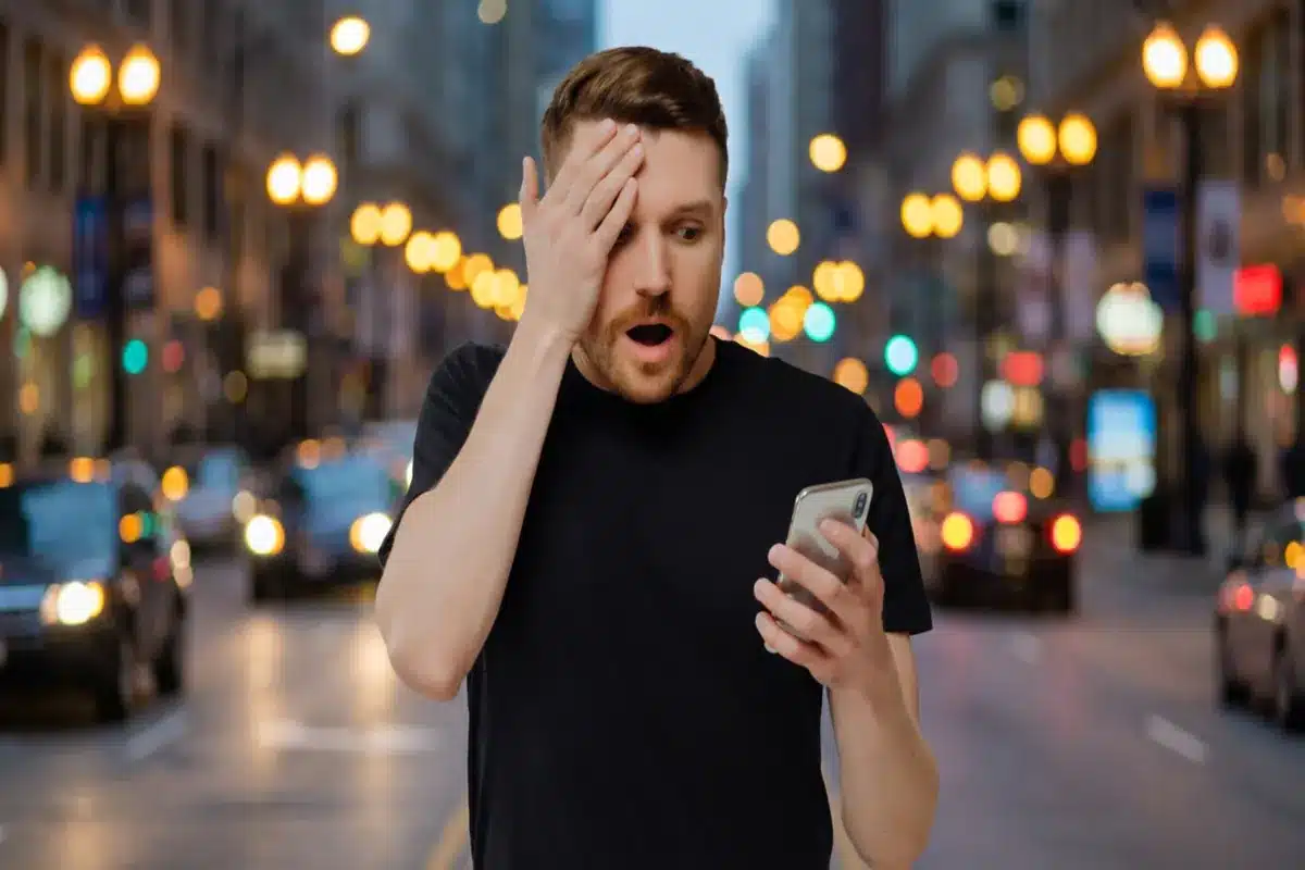Homem surpreso olhando o celular em ambiente urbano, representando os perigos de conexões Wi-Fi públicas automáticas.