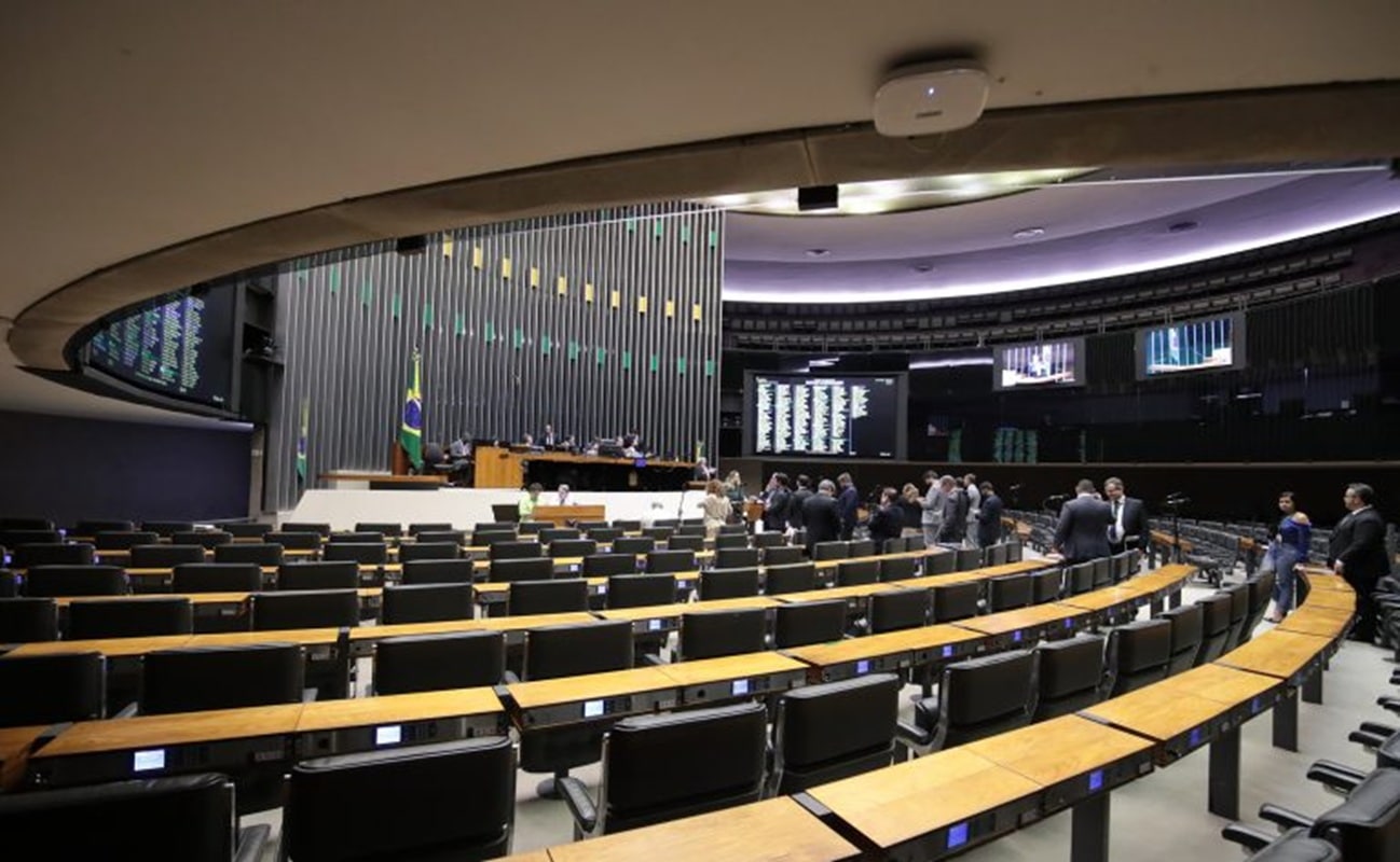 Plenário da Câmara dos Deputados em Brasília com cadeiras dispostas em semicírculo e bandeira do Brasil ao fundo