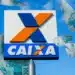 Fachada da CAIXA Econômica Federal com cédulas de 100 reais voando, representando a liberação do saque de R$ 6.220 para novas cidades