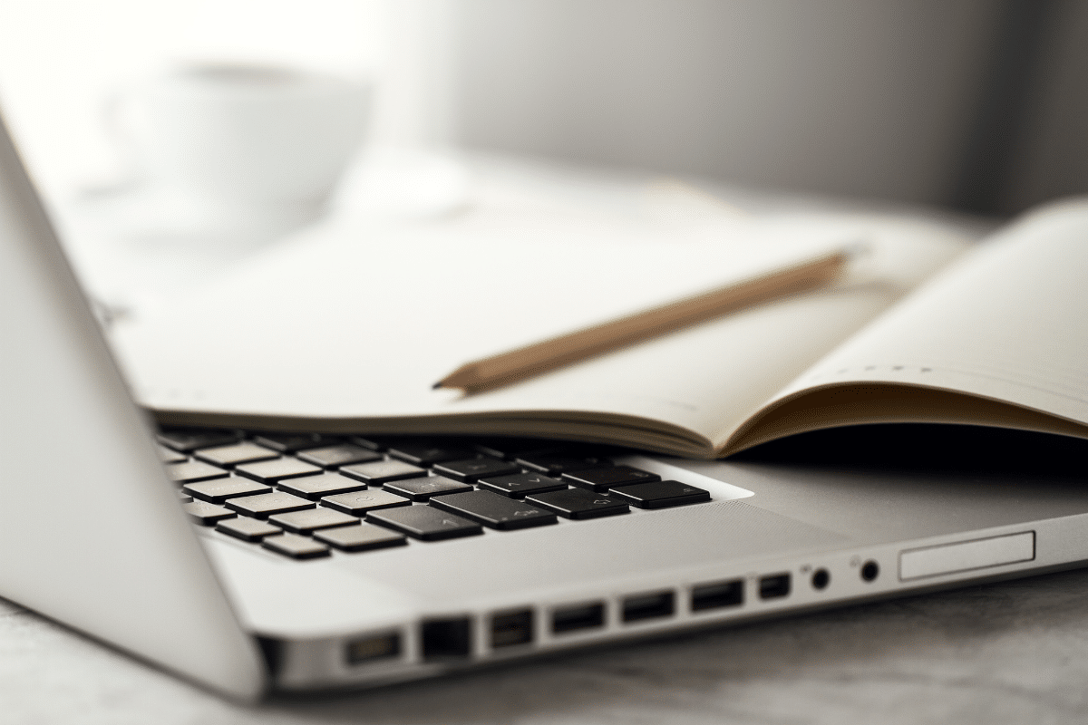 Laptop com teclado visível, caderno aberto e lápis apoiado sobre páginas
