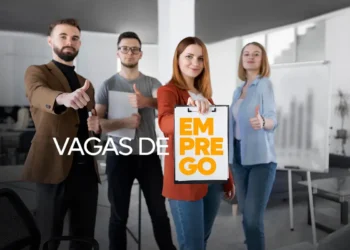 Quatro pessoas de negócios mostrando o sinal de positivo e segurando um cartaz de vagas de emprego em um ambiente de escritório moderno.