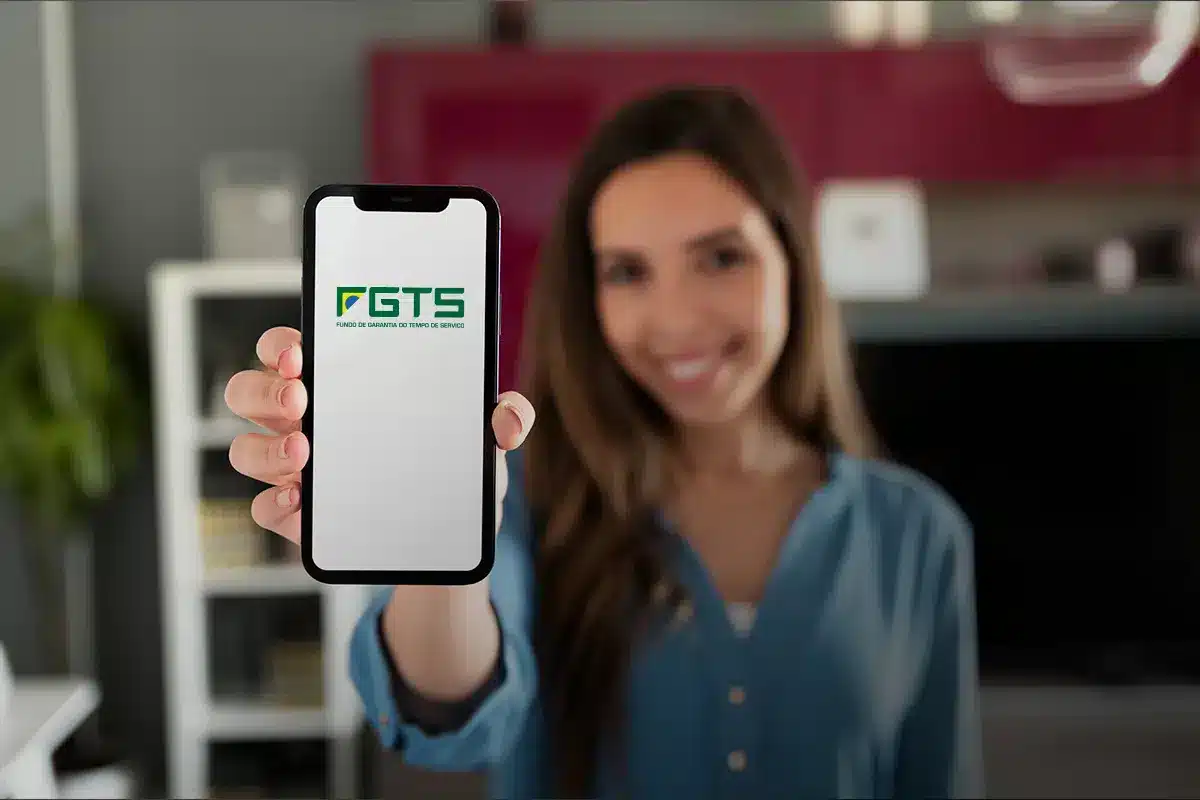 Mulher sorrindo e mostrando a tela do seu celular com a tela inicial do aplicativo do FGTS.