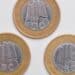 Fotografia de três moedas de 1 Real comemorativas dos 40 anos do Banco Central, organizadas em formato de triângulo sobre um fundo branco. A imagem exibe o lado do anverso das moedas, destacando os detalhes do núcleo prateado e as legendas douradas.