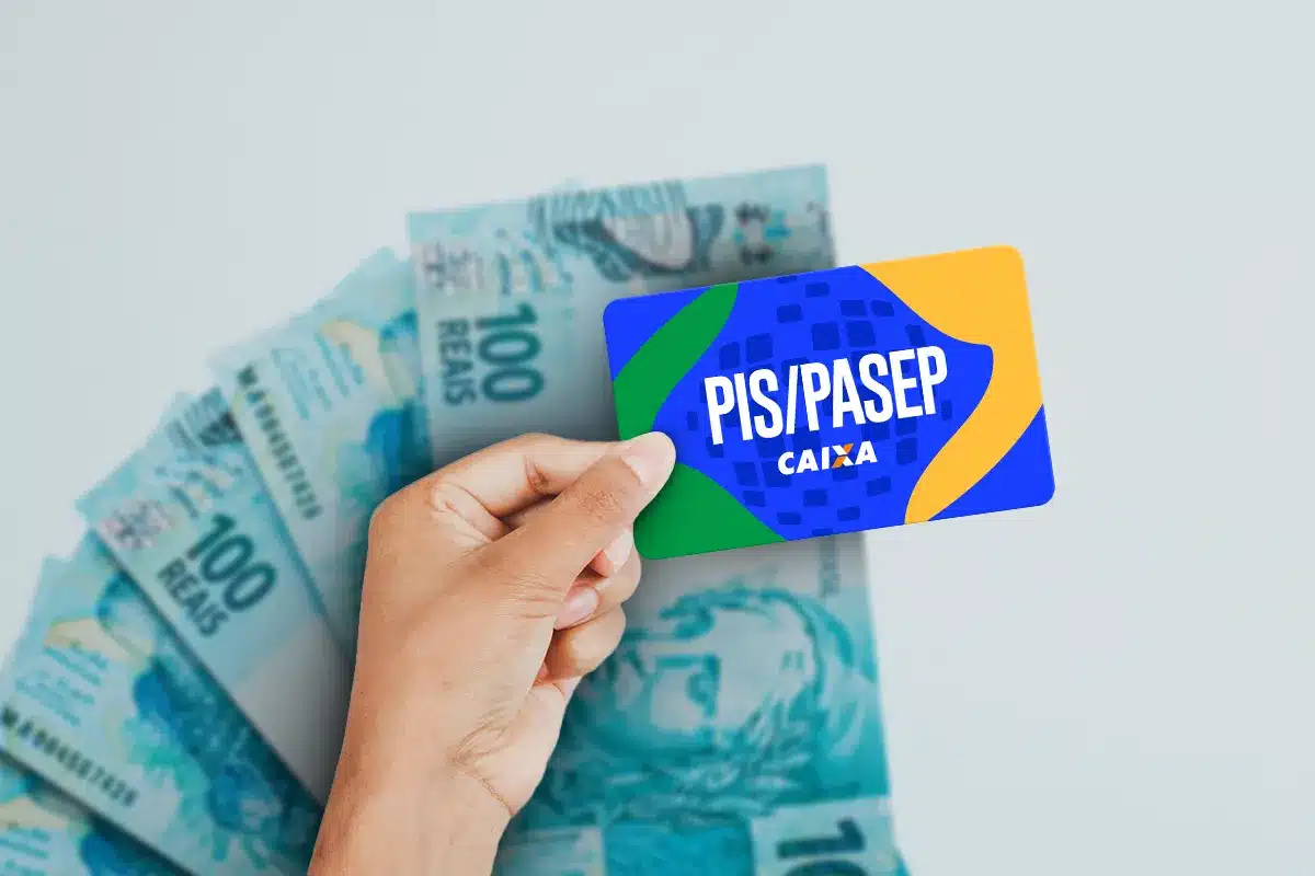 Mão segura cartão PIS/PASEP Caixa sobre várias cédulas de 100 reais