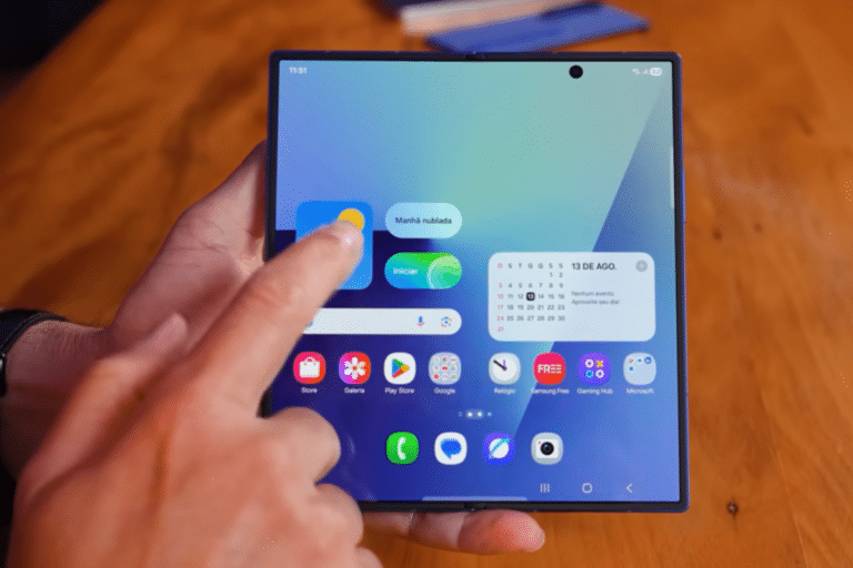 Mão interage com smartphone dobrável exibindo tela inicial e widgets
