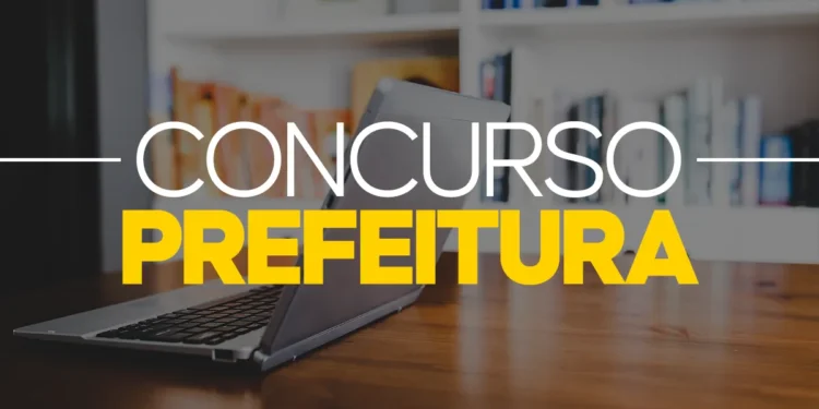 Laptop aberto sobre uma mesa de madeira com o texto "CONCURSO PREFEITURA" em destaque nas cores branco e amarelo, com uma estante de livros ao fundo.