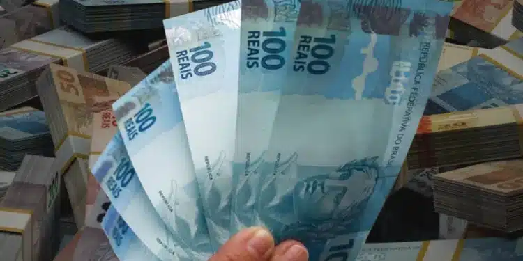Notas de real brasileiro seguradas na mão, representando pagamentos da Caixa Econômica Federal para CPFs com final de 0 a 9.