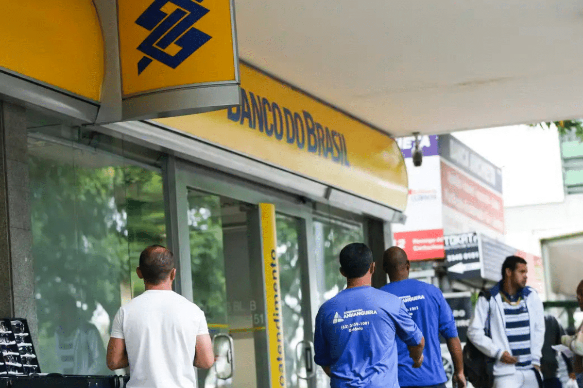 Pessoas caminhando e aguardando diante da agência do Banco do Brasil em área urbana