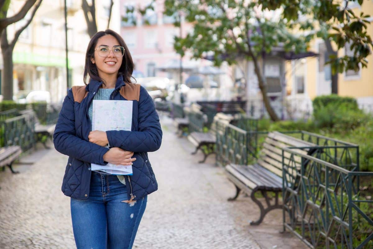Estudante universitária caminhando ao ar livre segurando caderno enquanto pensa sobre futuro profissional e escolhas de carreira.