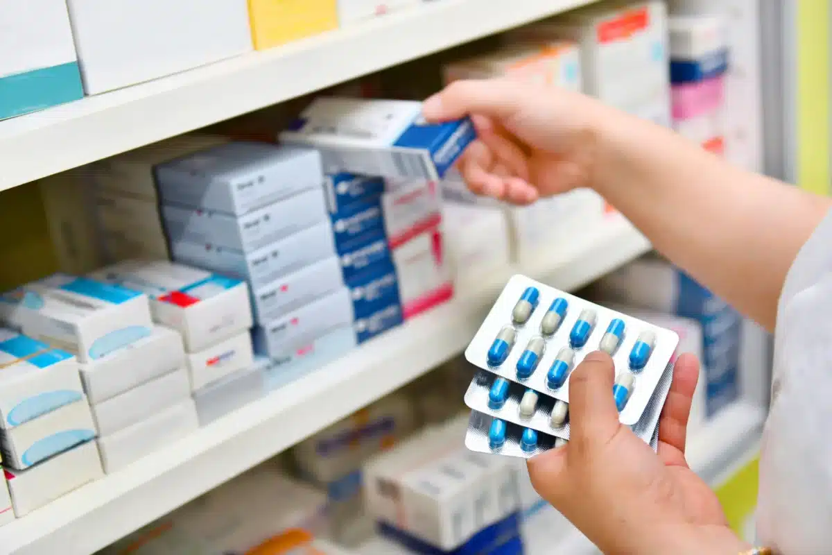 Farmacêutico selecionando medicamentos em uma prateleira, com destaque para caixas e cartuchos de remédios, ilustrando o contexto de possíveis reajustes de preços no Brasil.
