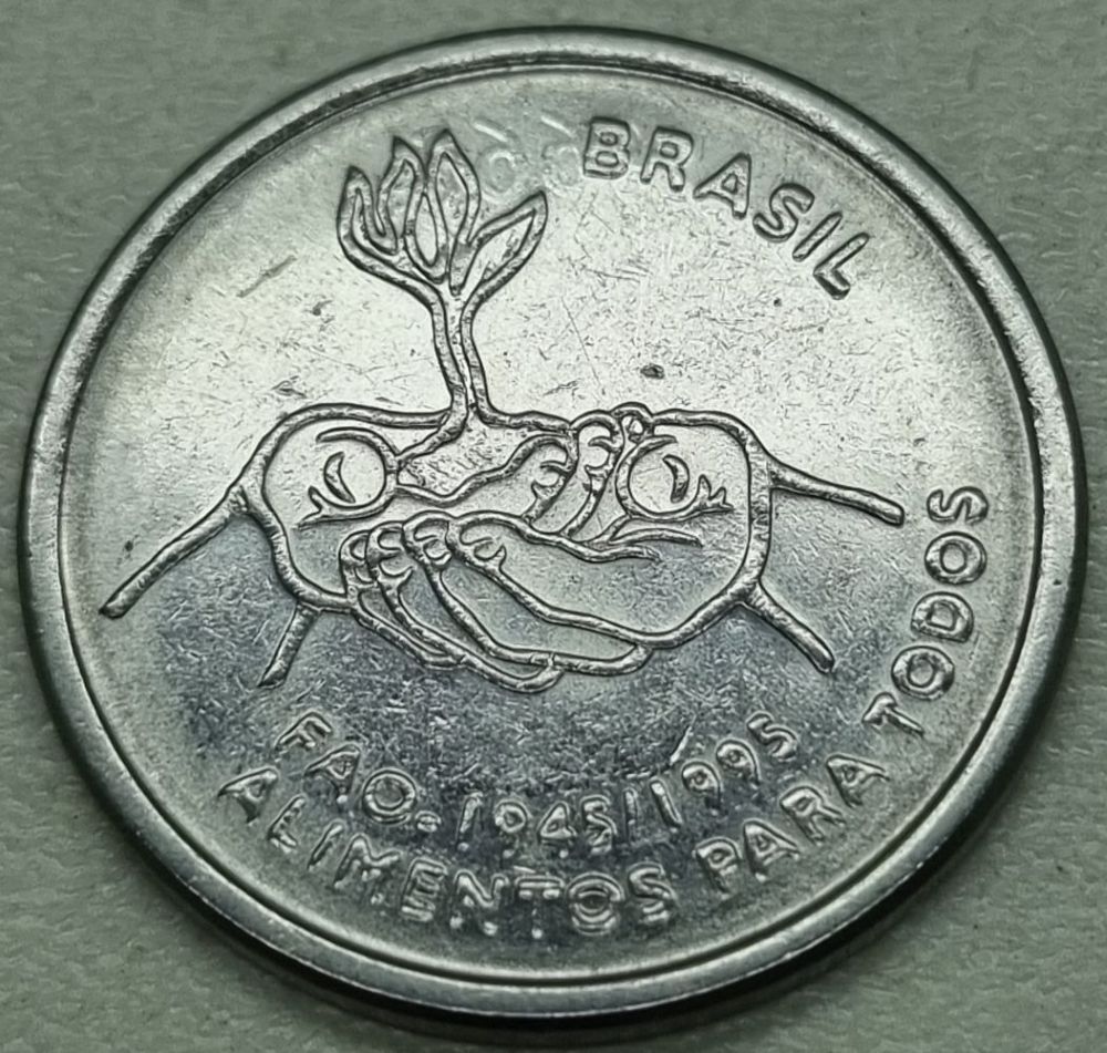 Close-up de uma moeda de 10 centavos de 1995 (edição FAO), com foco nos detalhes do desenho de mãos segurando um broto e a inscrição 'Alimentos para Todos'.