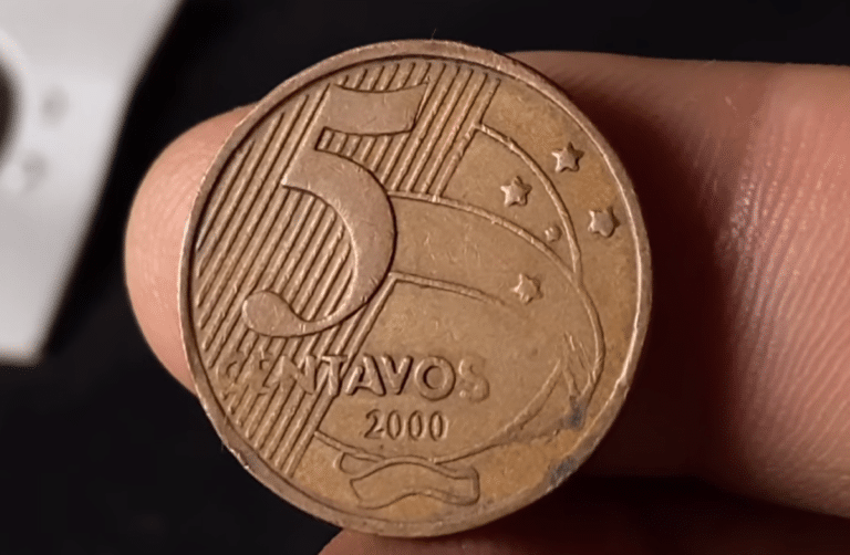 Close do reverso de uma moeda de 5 centavos do ano 2000, de cor bronze, sendo segurada por dedos. O foco está nos detalhes do cunho e na data.