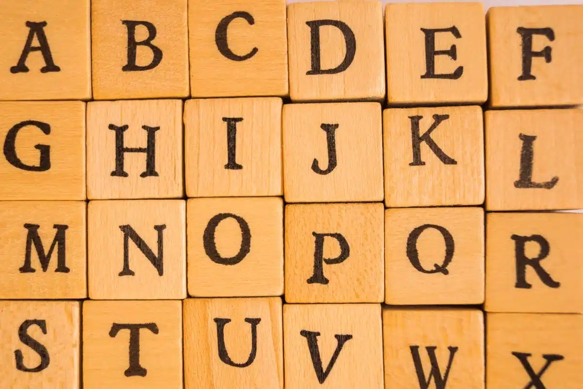 Letras do alfabeto em blocos de madeira representando exemplos de palavras invariáveis no plural na língua portuguesa