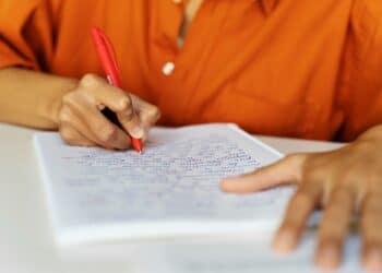 Pessoa fazendo anotações com caneta vermelha em caderno quadriculado representando candidato se preparando para o processo seletivo da Prefeitura de Mansidão BA