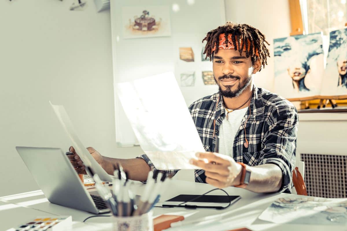 Homem jovem com cabelo escuro e bandana, segurando papéis em ambiente de trabalho criativo, refletindo sobre áreas artísticas relacionadas ao signo de Peixes.