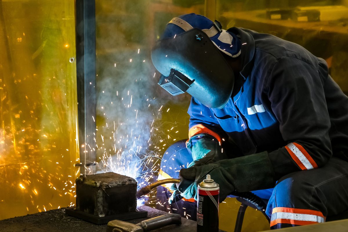 Soldador industrial utilizando técnica MIG/TIG durante processo de soldagem em ambiente metalúrgico.