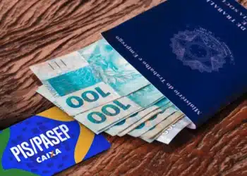Dinheiro em notas de R$ 100 com carteira de trabalho e cartão PIS/PASEP sobre superfície de madeira