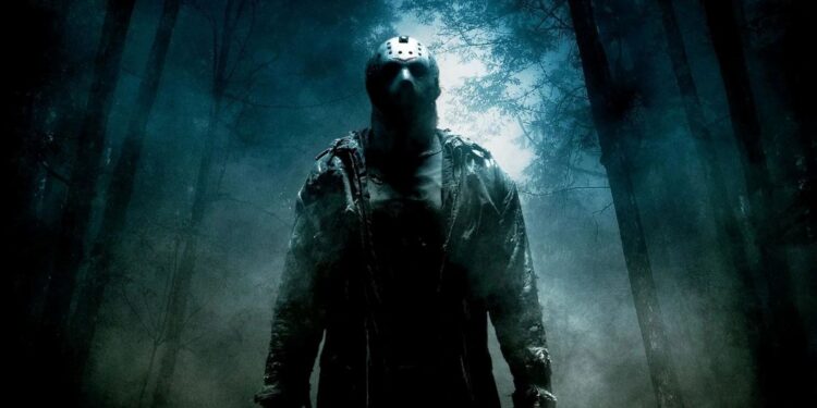 Figura sombria do personagem Jason Voorhees, de Sexta-Feira 13, usando sua icônica máscara de hóquei. Ele está em pé em uma floresta nebulosa e escura à noite, iluminada por uma luz azulada vinda de trás das árvores.