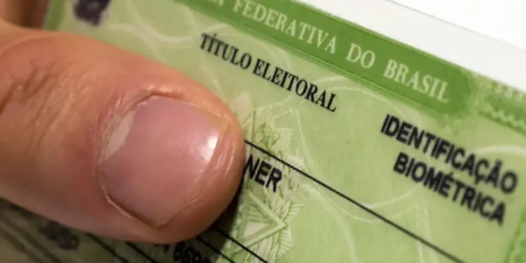 Close de um título de eleitor brasileiro com identificação biométrica sendo segurado por uma pessoa, representando o prazo para emissão do primeiro documento eleitoral.