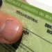 Close de um título de eleitor brasileiro com identificação biométrica sendo segurado por uma pessoa, representando o prazo para emissão do primeiro documento eleitoral.