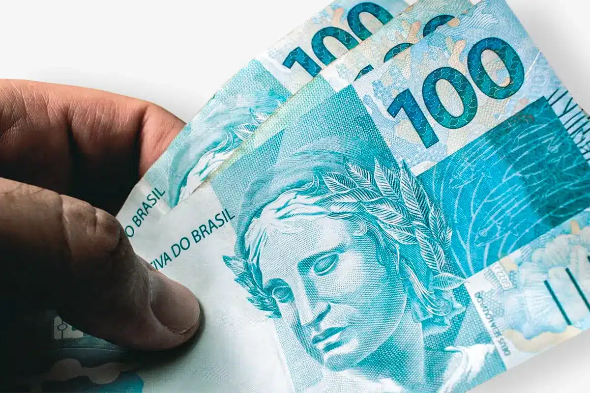 Notas de R$ 100 sendo seguradas por uma mão, ilustrando o benefício de R$ 300 do programa Mães de Pernambuco.