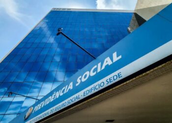 Fachada moderna da sede da Previdência Social com logo do INSS em destaque e céu azul ao fundo.