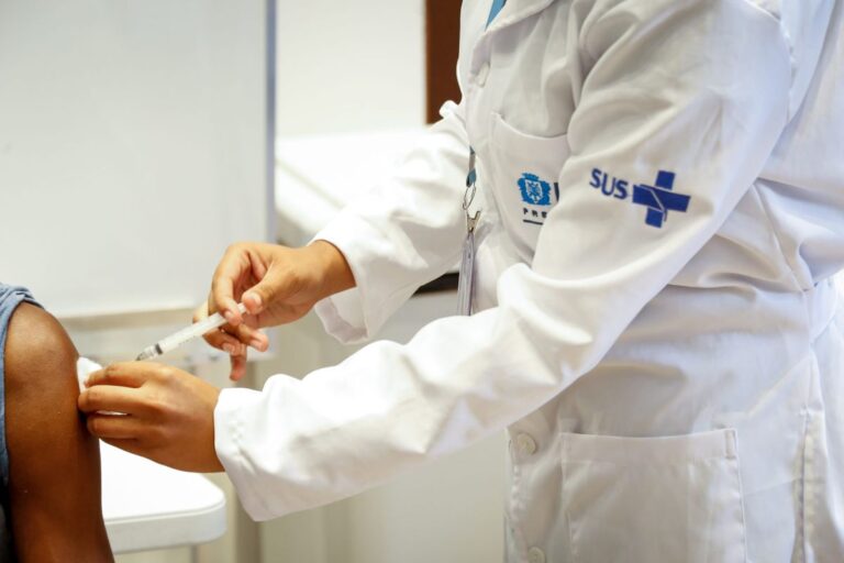 Profissional de saúde aplicando vacina em um paciente, com uniforme do SUS, durante a Semana de Vacinação nas Américas.