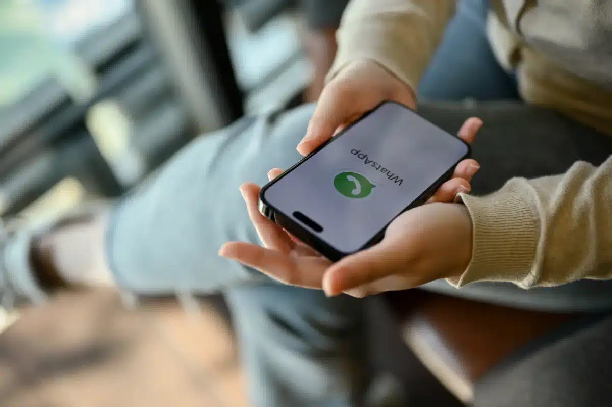 Pessoa segurando smartphone com WhatsApp aberto, ilustrando como evitar mensagens de listas de transmissão.