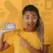 Pessoa mostrando celular destacando a tela com o logo Pé-de-Meia e título sobre poupança escolar, representando o acesso à conta do benefício