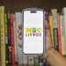 MEC Livros biblioteca digital gratuita - mão segurando smartphone com logo MEC Livros em frente a estante de livros