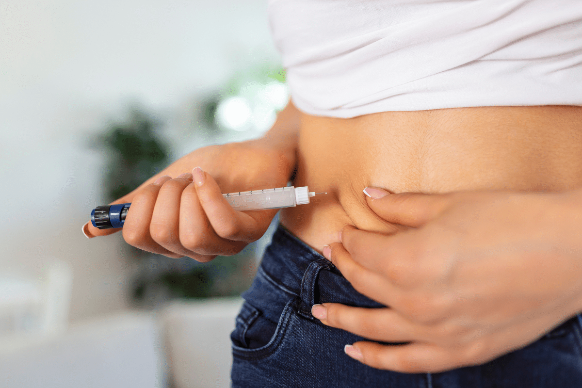 Pessoa segura caneta de insulina próximo à barriga, fazendo prega subcutânea para aplicação
