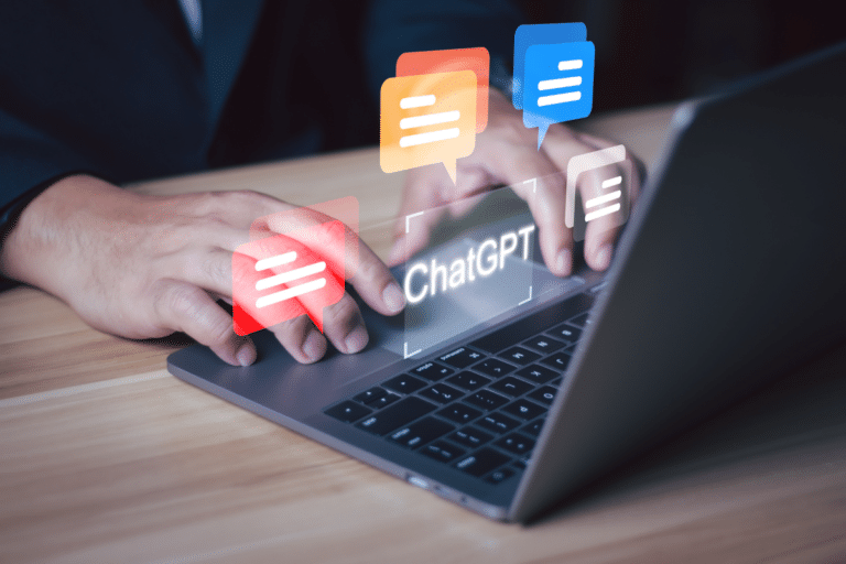 Pessoa digitando em laptop cinza com balões de conversa coloridos e texto "ChatGPT" na tela