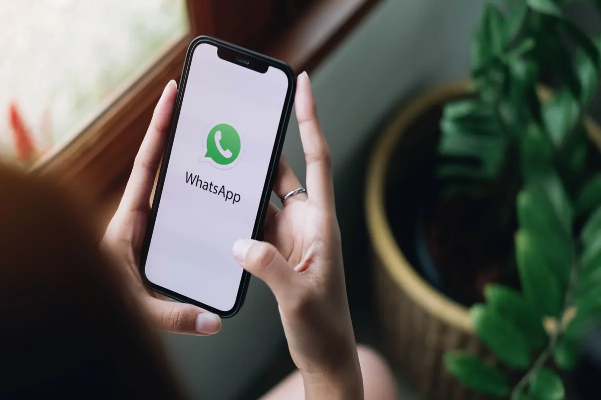 Usuário segurando smartphone com WhatsApp aberto, representando o risco de exposição de dados pessoais durante compartilhamento de tela.