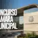 Prédio de Câmara Municipal moderno com fachada de vidro, brasão metálico, espelho d'água frontal e céu azul