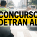 Agente de trânsito com colete verde DETRAN sinaliza parada com o braço estendido em via urbana congestionada