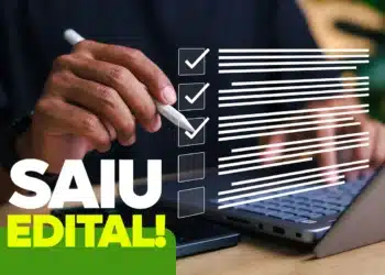 Mão segurando caneta branca em frente a notebook com checklist virtual e texto "Saiu Edital!" em destaque.