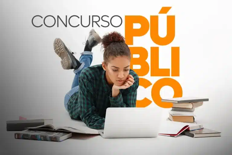 Jovem deitada no chão estudando em notebook ao lado de pilha de livros para concurso público