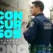 Guarda Municipal de uniforme azul-marinho segura rádio comunicador em rua de paralelepípedos com prédios coloniais ao fundo.