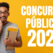 Jovem negro de óculos segura cadernos e apostilas com expressão de surpresa, fundo amarelo com texto "Concursos Públicos 2026".