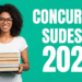 Jovem de óculos e cabelos cacheados segura livros, ao lado de texto "Concursos Sudeste 2026" em fundo verde