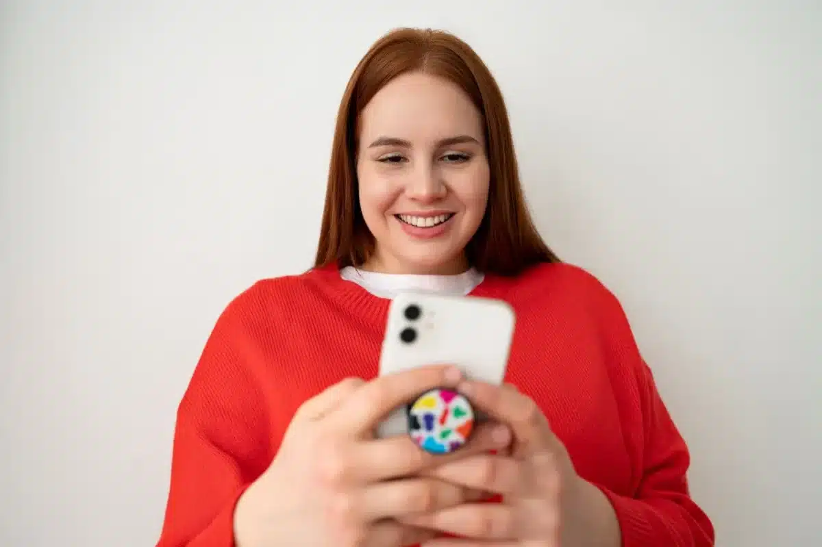 Mulher sorrindo e usando um smartphone com pop socket, criando figurinhas no WhatsApp.