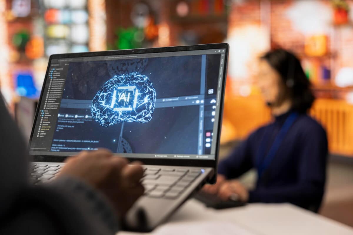 Tela de notebook exibe representação gráfica de um cérebro digital com a inscrição "AI", simbolizando o uso da inteligência artificial no ambiente corporativo.