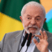 Presidente Lula gesticula durante pronunciamento com terno cinza, camisa azul e bandeiras do Brasil ao fundo