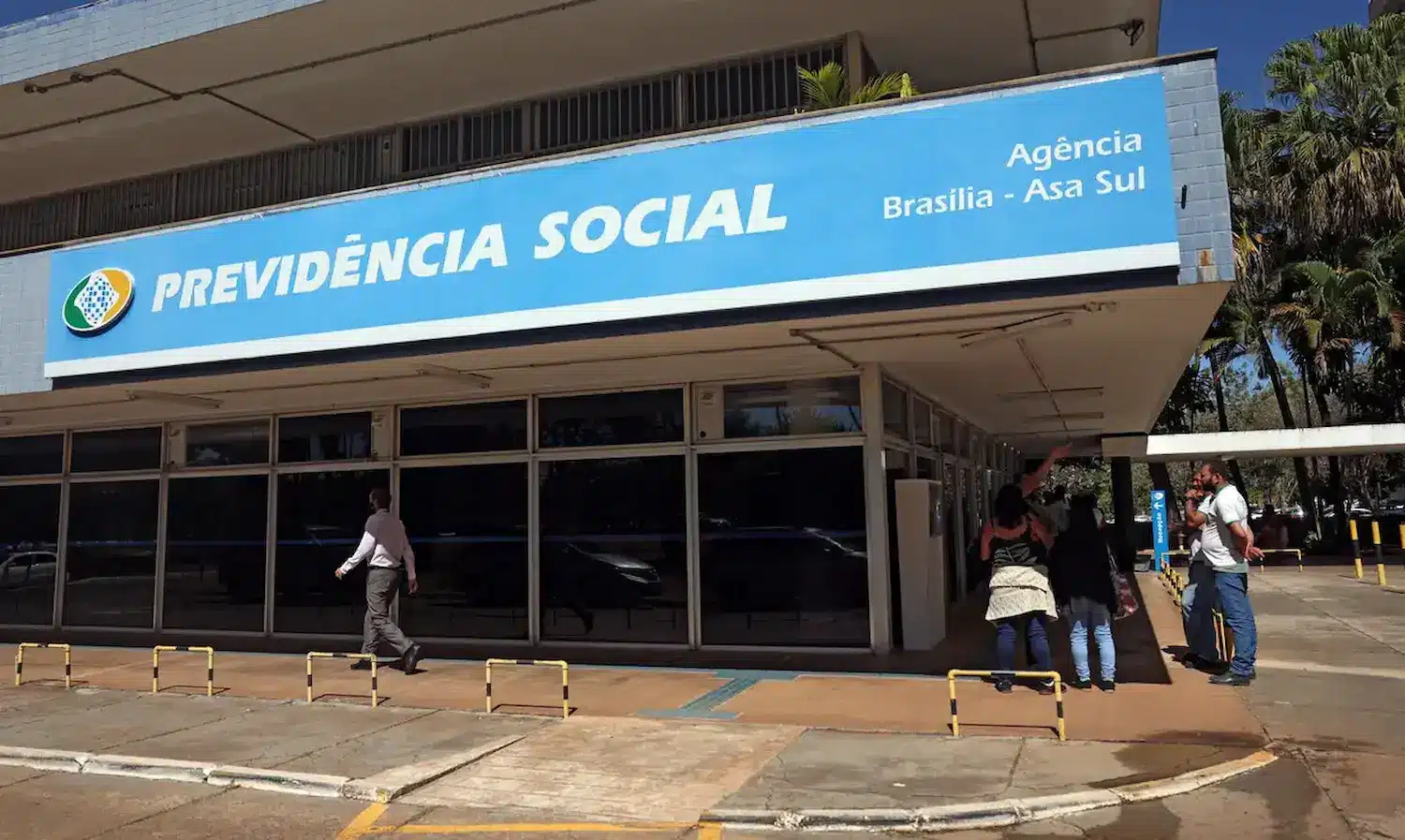 Agência da Previdência Social em Brasília, mostrando a fachada do prédio com pessoas na entrada e o logotipo visível.