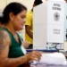 Imagem de mesários durante o processo eleitoral, com foco em uma cabine de votação e pessoas interagindo em uma seção eleitoral.