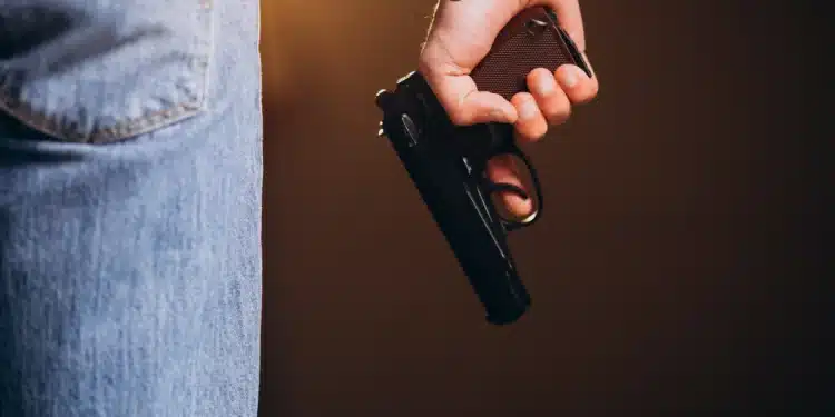 Pessoa segurando arma de fogo ao lado do corpo, representando profissões com autorização de porte no Brasil.