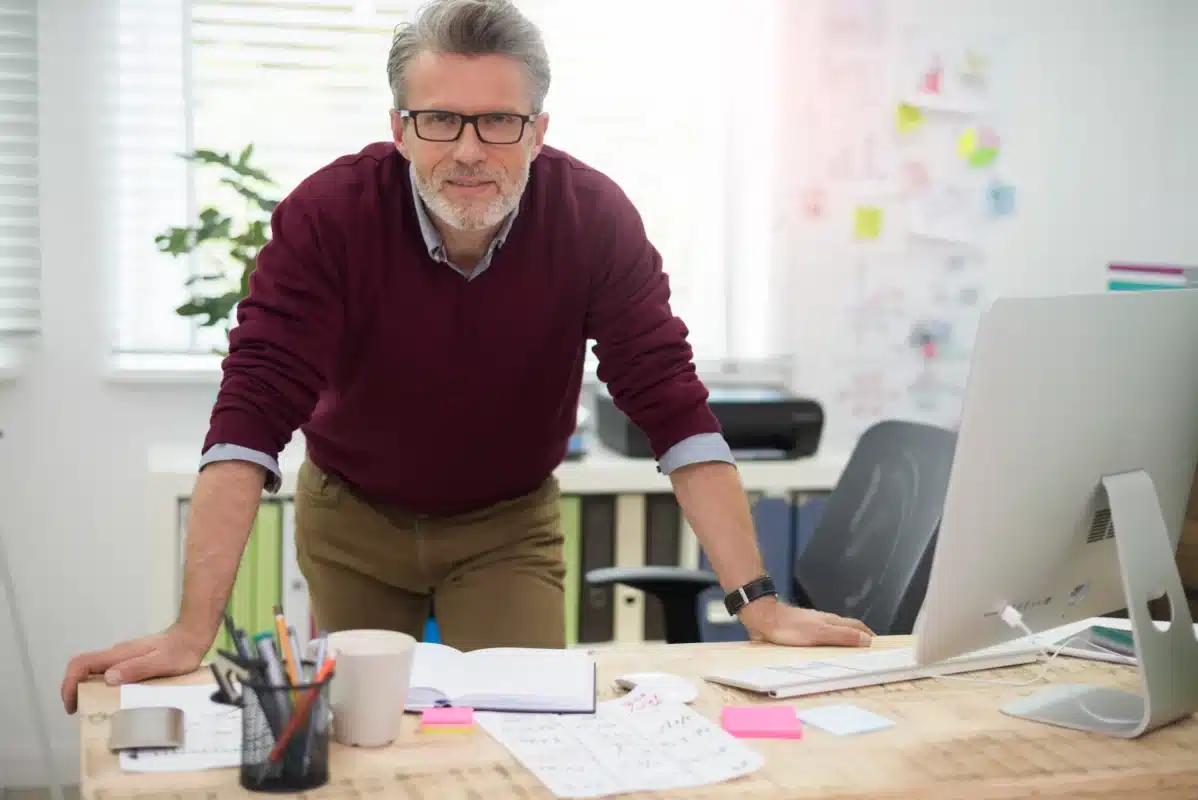 Profissional experiente com mais de 50 anos trabalhando em escritório moderno e demonstrando liderança no ambiente corporativo.